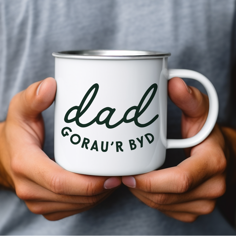 Person holding a white mug with 'dad Gorau'r Byd' text, wearing a gray shirt.